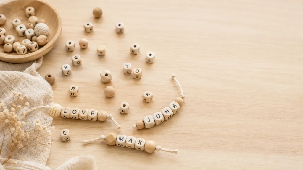Buchstabenperlen liegen verstreut auf hellem Holztisch, einzelne Wörter („MAMA", „LEO") sind aufgefädelt sichtbar.
